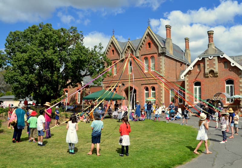 Children maypole dancing with colourful ribbons on the lawn outside the heritage school building at the Spring Fair